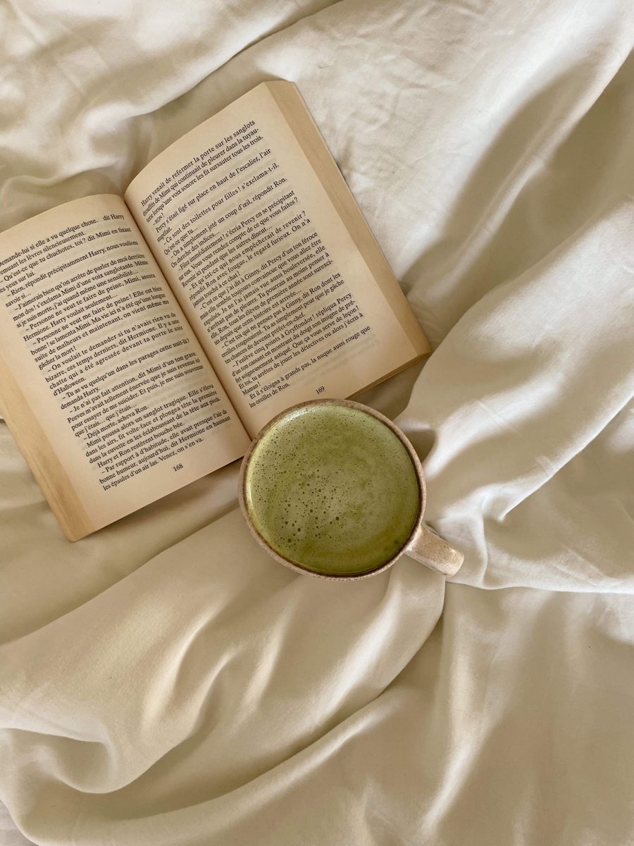 A cup of matcha on a bedsheet with an open book